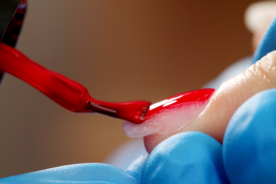 Une prothésiste ongulaire vernissant les mains de sa cliente en respectant les consignes de santé des doigts en matière de vernis semi-permanent