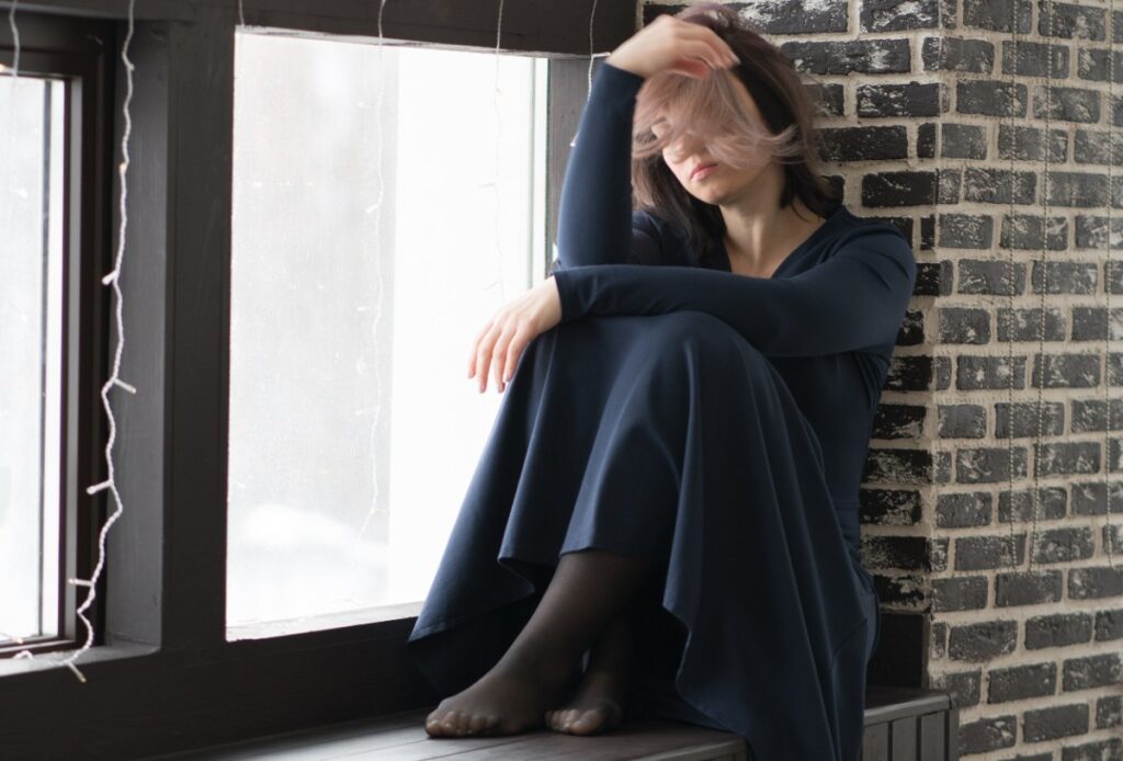 Une femme assise sur la fenêtre et met du collant sous sa robe bleu marine