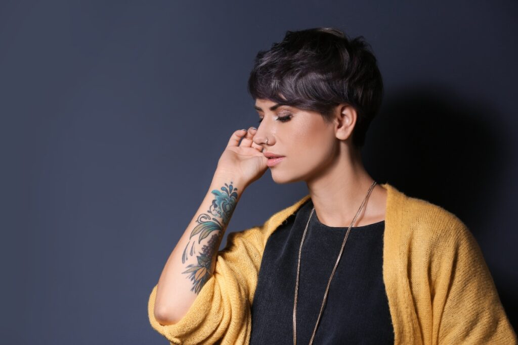 Une femme aux cheveux courts avec un tatouage sur son bras et portant un cardigan jaune