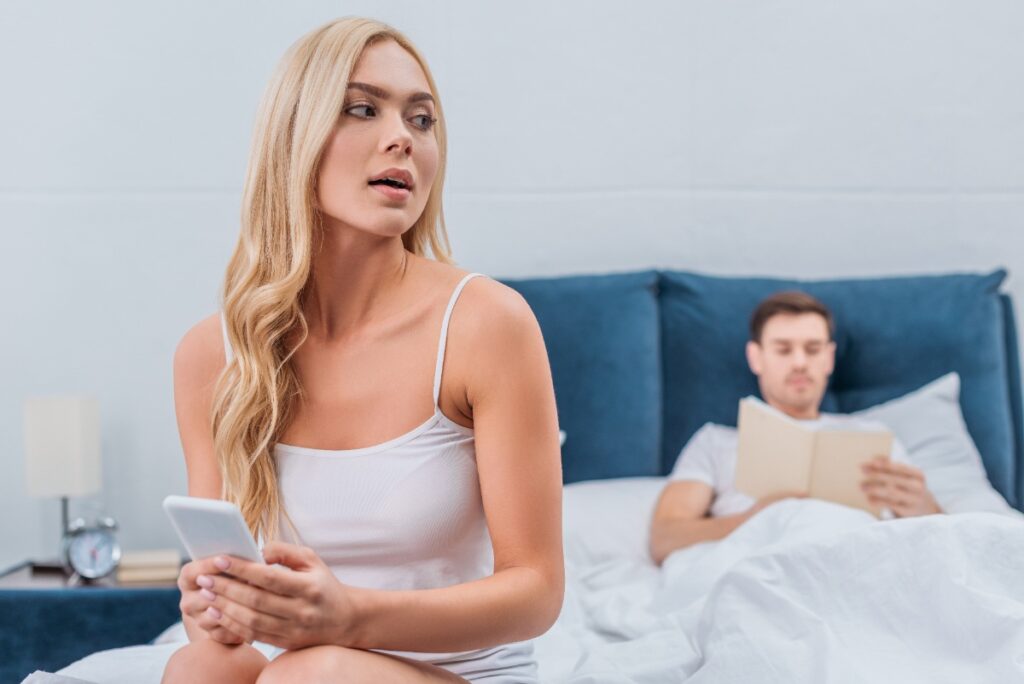 Une femme qui utilise son téléphone devant son homme au lit